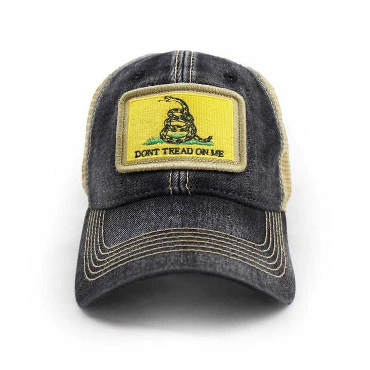 Black trucker hat with khaki mesh back panels and tan stitching laying. Ballcap is embroidered with a patch of the Gadsden flag, the patch has a yellow background with a snake coiled in grass and the words Don't Tread On Me